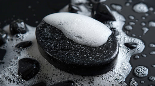 A black oval soap placed on a pile of large gravel, with an entirely black background. The background features large stones, smoke and plays of light and shadow.